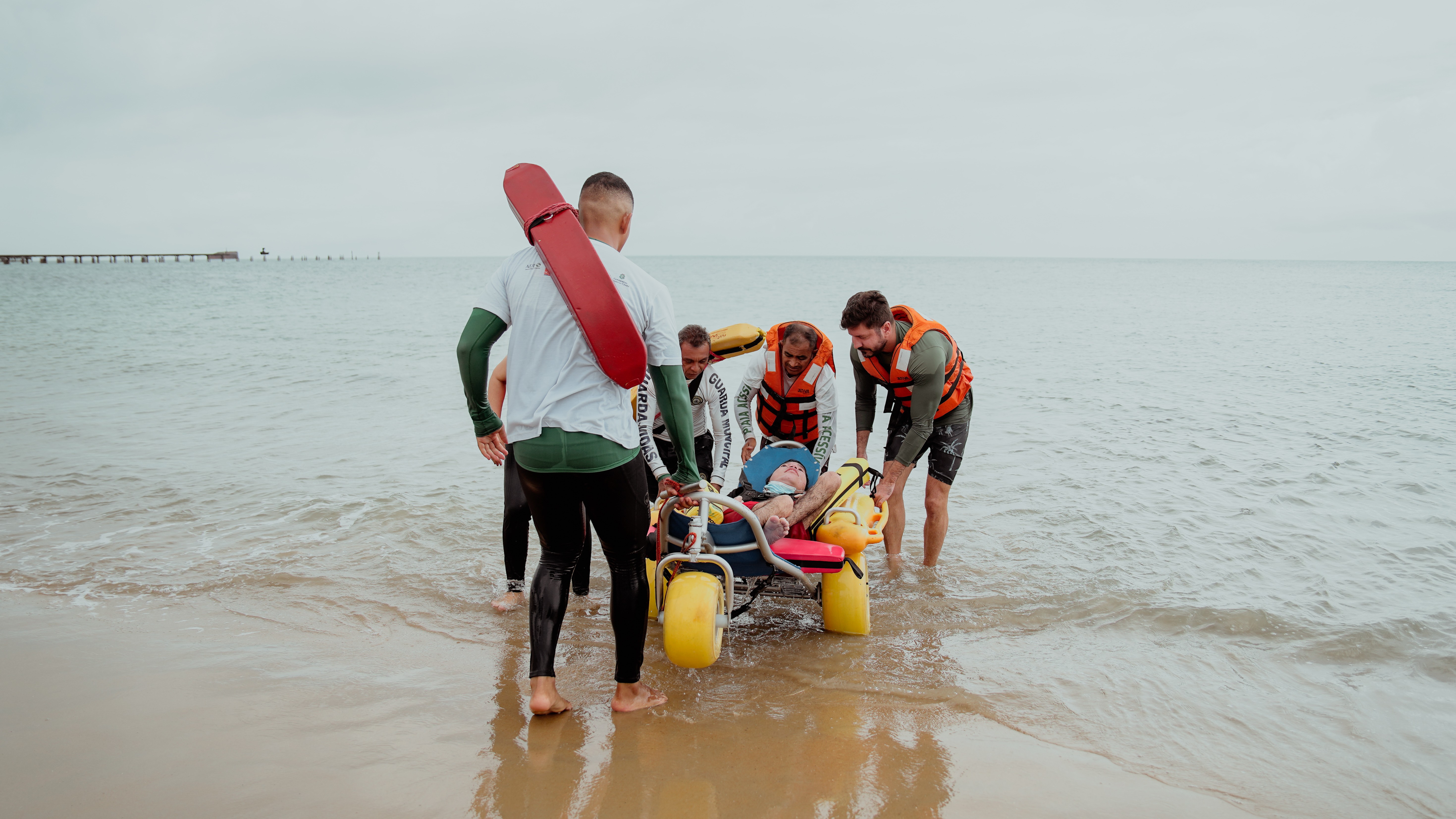 guarda-vidas levando um jovem com paralisia cerebral em um carro adaptado para entrar no mar